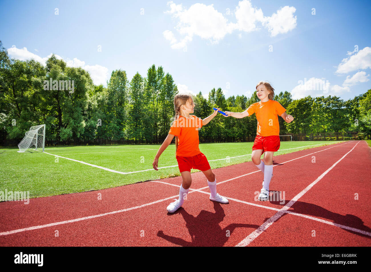 Running girl with baton hands it to other runner Stock Photo
