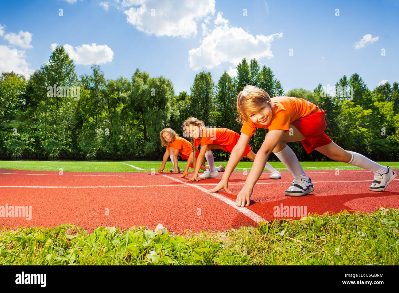 Three smiling children in ready position to run Stock Photo