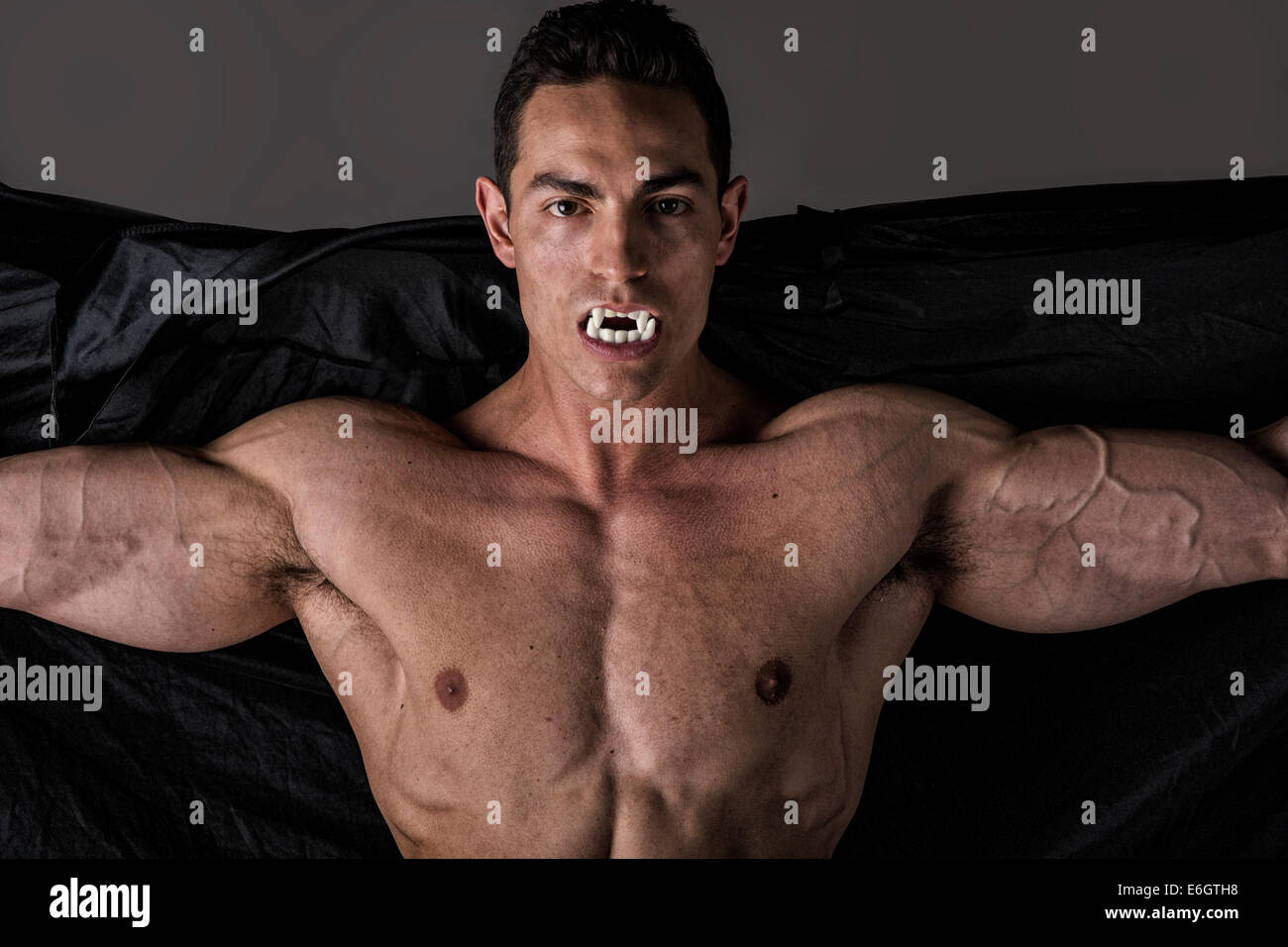 Naked muscular fit young man posing as a vampire or Dracula in a black  cloak showing off his powerful body bearing his fangs Stock Photo - Alamy