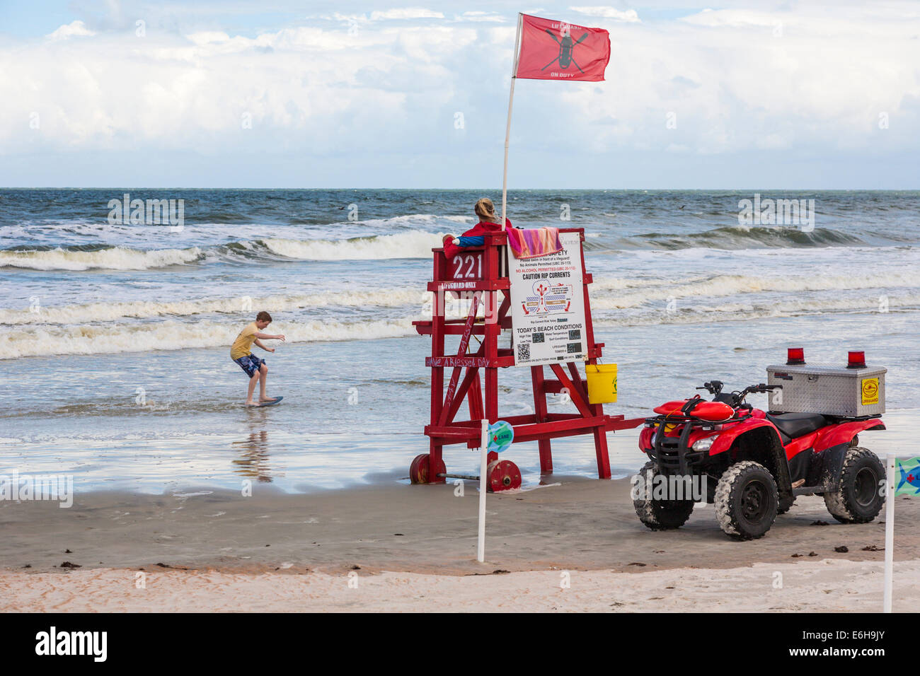 Lifeguard watches over young boy playing with skim board in the surf at Daytona Beach, Florida Stock Photo