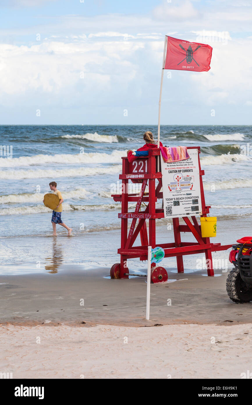 Lifeguard watches over young boy playing with skim board in the surf at Daytona Beach, Florida Stock Photo