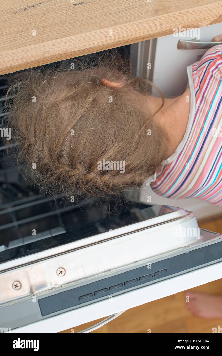 Little girl putting head into dishwasher. Dangerous situation at home