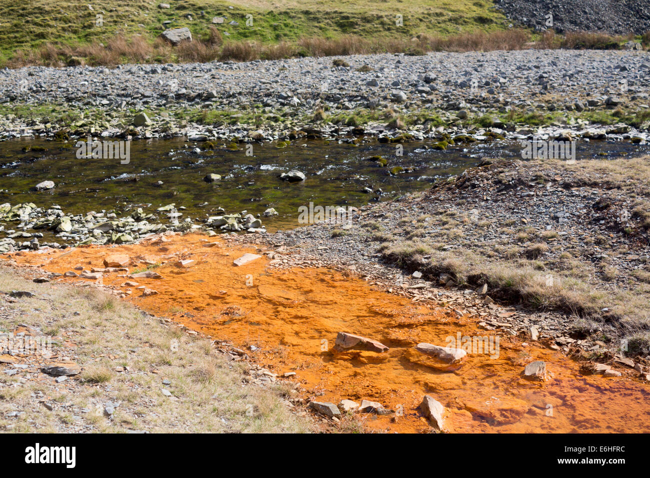 Polluted contaminated water flowing from stream from abandoned lead mine into river with clean water Cwmystwyth Mid Wales UK Stock Photo