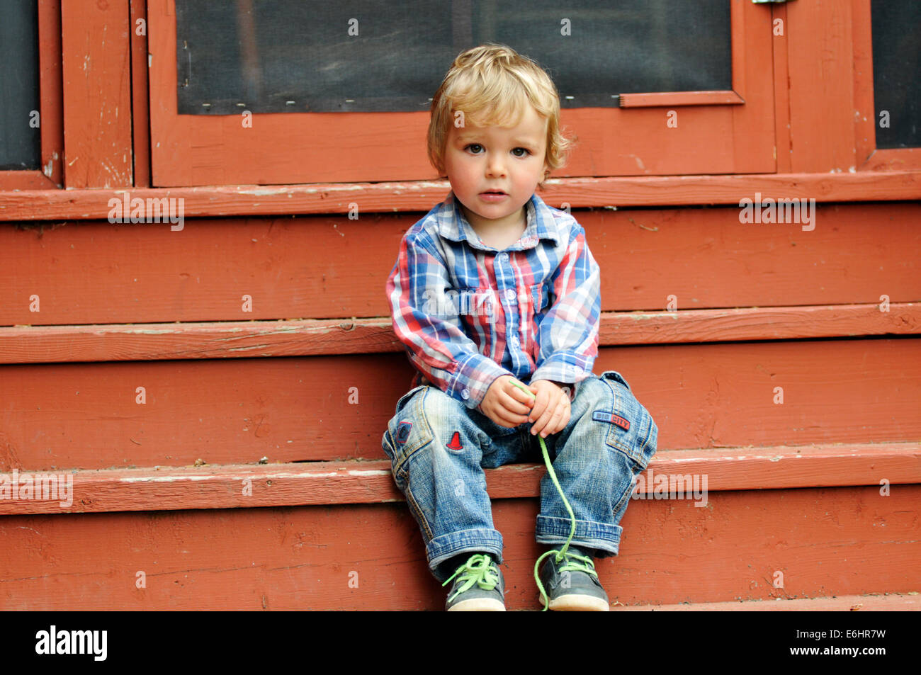 A young boy sat on the steps of a house undoing his laces Stock Photo