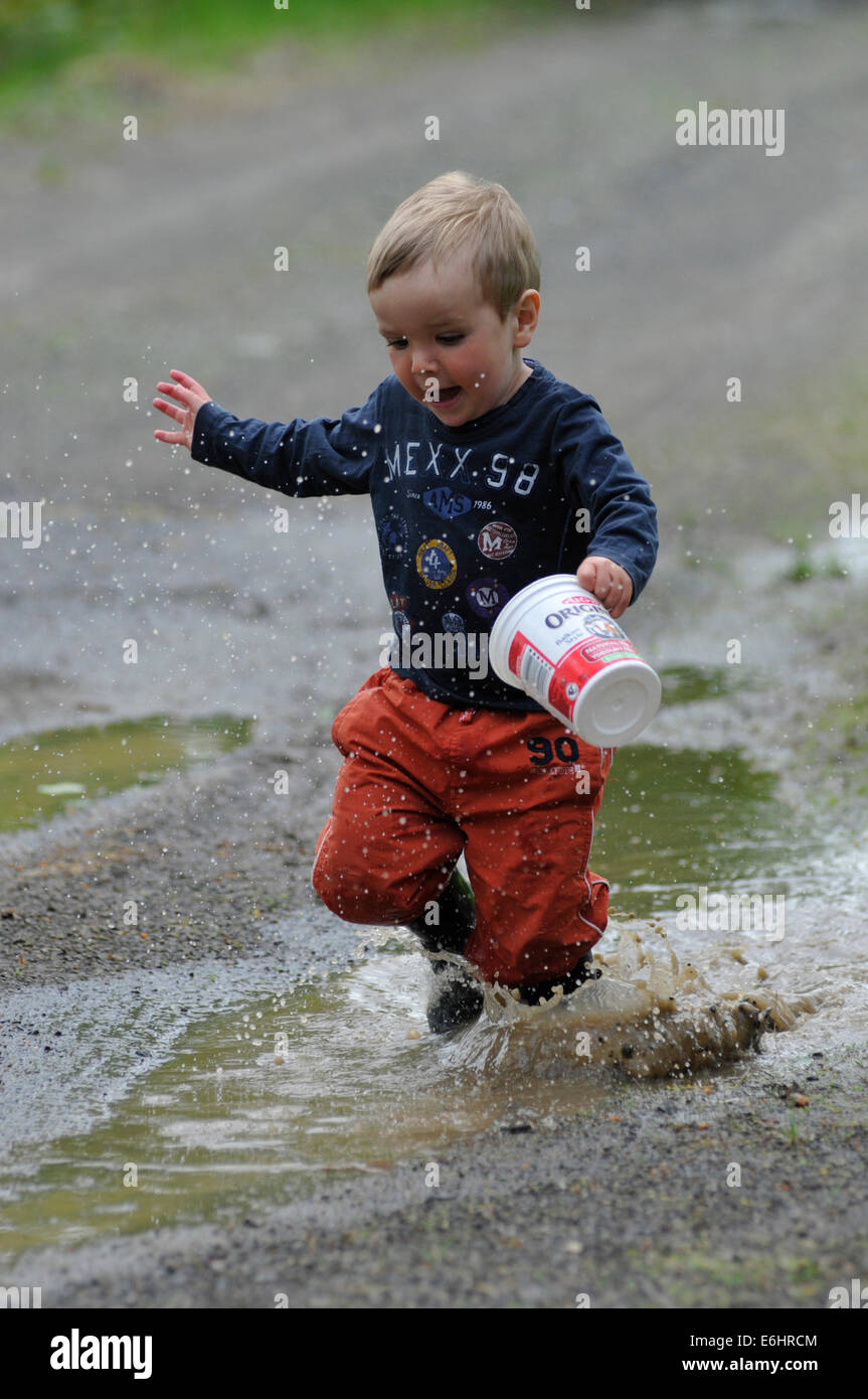 A young boy getting soaked running through a puddle Stock Photo