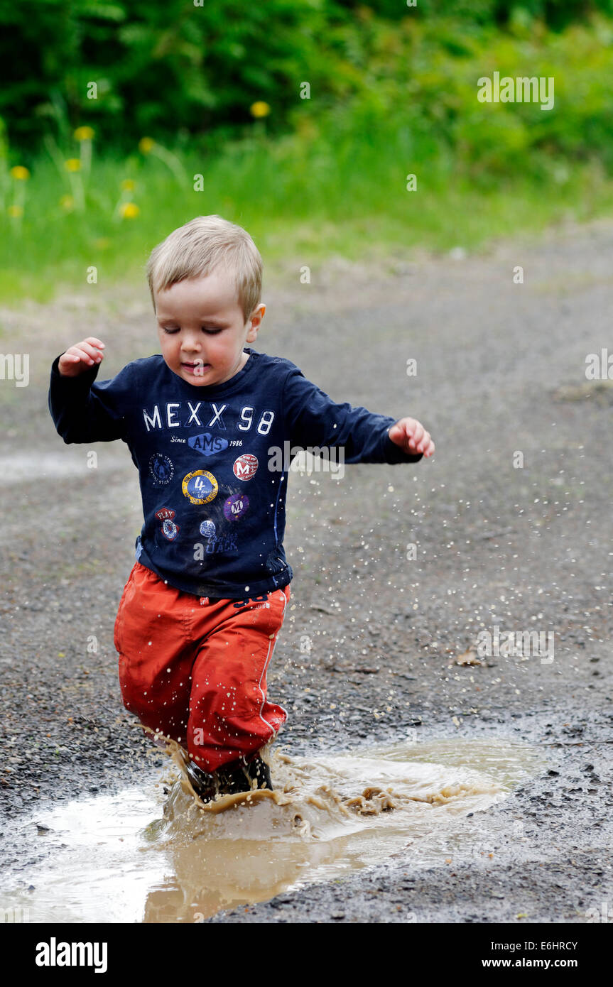 A young boy getting soaked running through a puddle Stock Photo