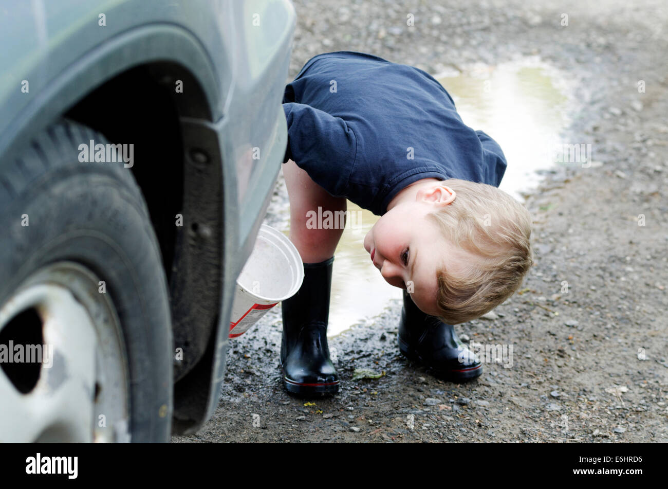 A little boy bending to look under a car Stock Photo