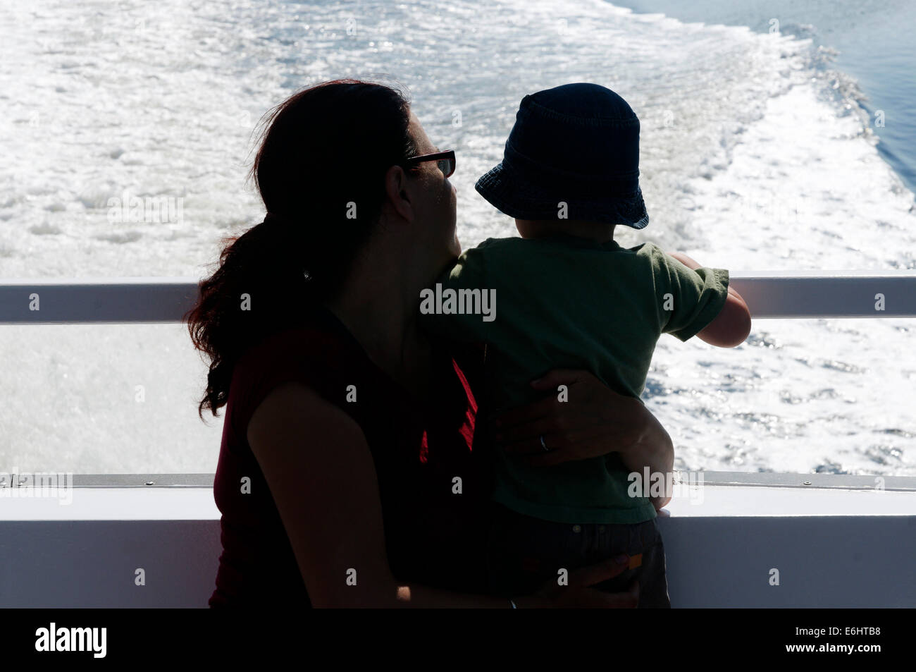 A mother and son silhouetted against the wake of a boat on a summer cruise Stock Photo