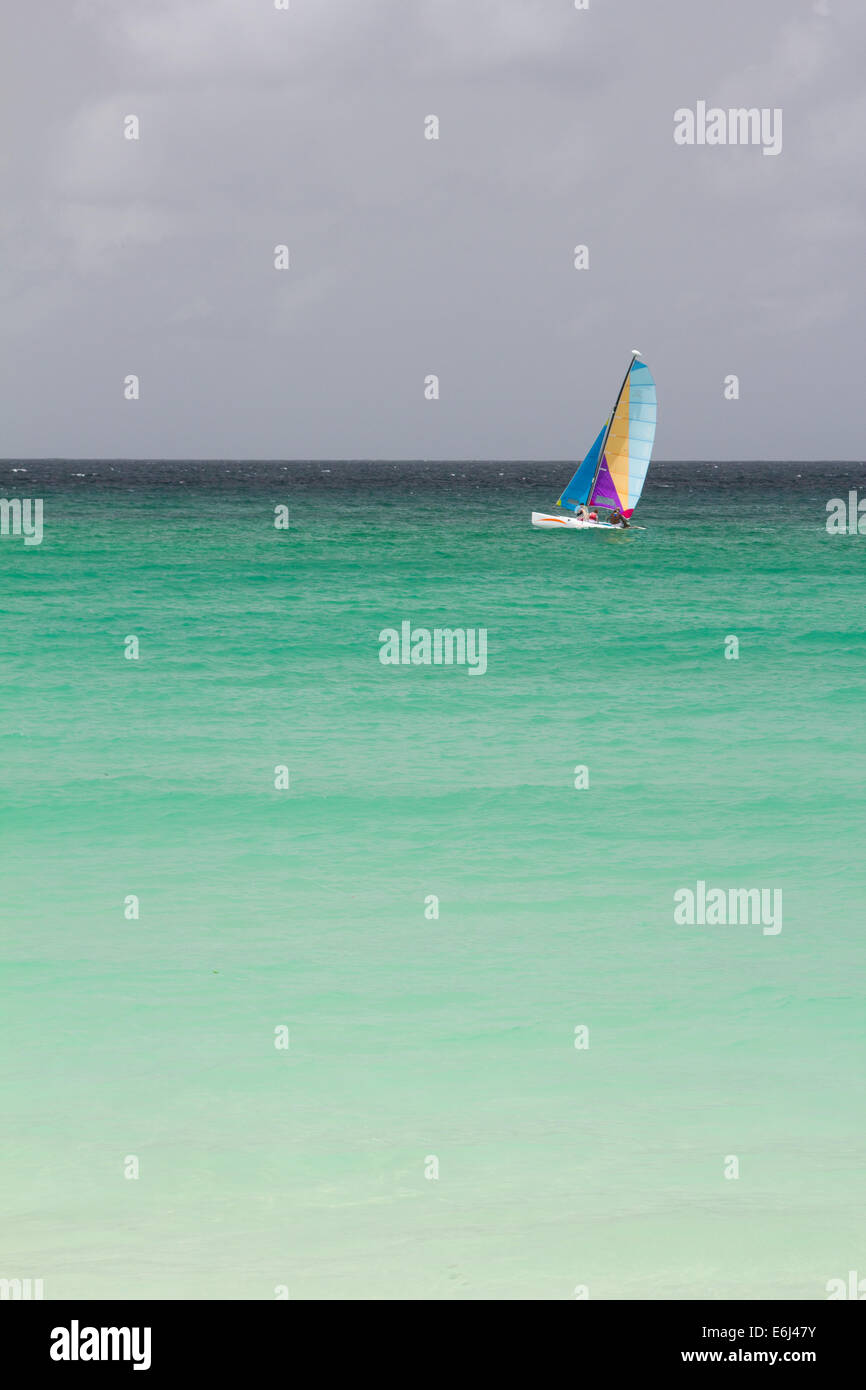 Sailing boat on a turquoise sea against a dark moody sky in Barbados Stock Photo
