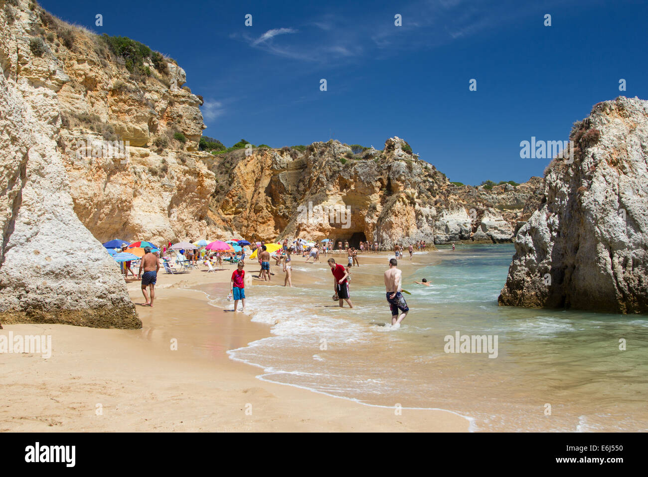 People enjoying a sunny day on the beach in Alvor Portugal, the beach is sheltered by sandstone cliffs. Stock Photo