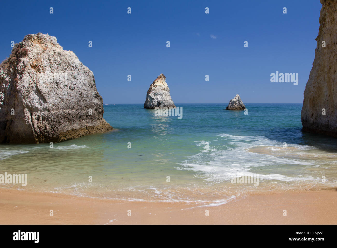Sea view Alvor Portugal with golden sand and blue sky there are three large rocks in the foreground. Stock Photo