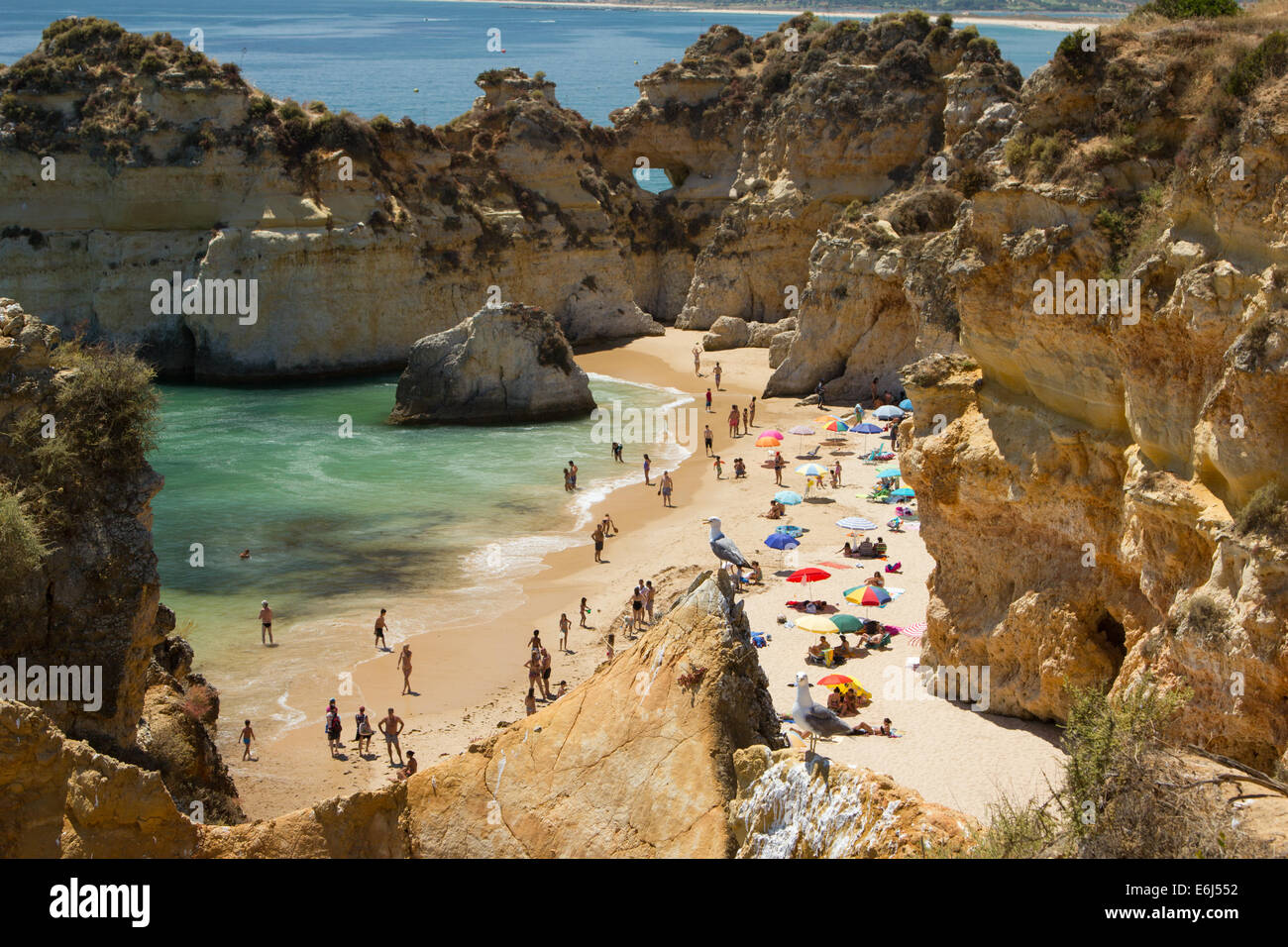 People enjoying a sunny day on the beach in Alvor Portugal, the beach is sheltered by sandstone cliffs. Stock Photo