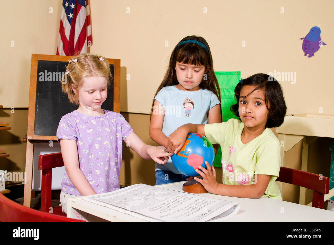 multi ethnic racial diversity diverse multicultural group 4-5 year old Girls person people map kindergarten classroom eye contact looking globe table Stock Photo