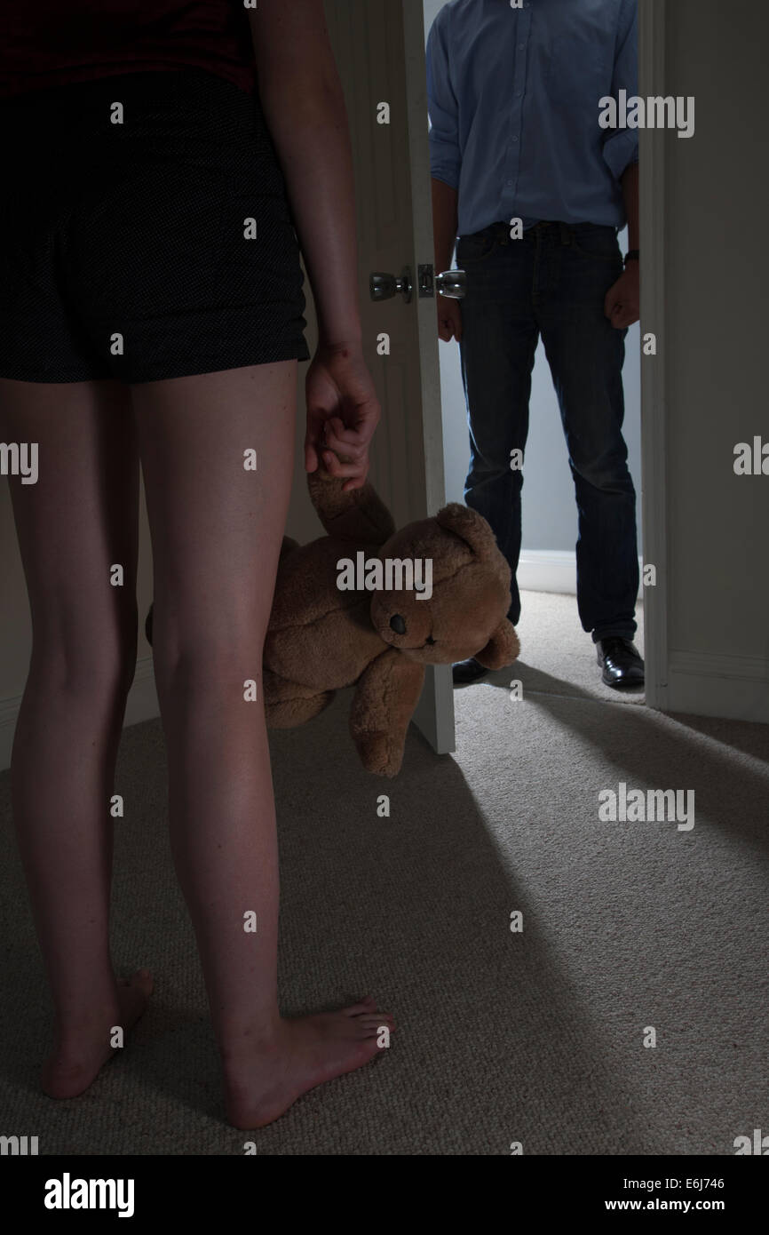 Anonymous man entering a dark room, a young girl standing in the foreground looking towards the man holding a teddy-bear. Close. Stock Photo