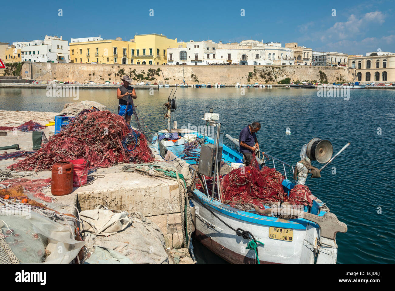 cleaning old fishing nets Fishermen mending fishing nets and cleaning boats at the quay in the old  town of Gallipoli, Puglia, Southern Italy Stock Photo