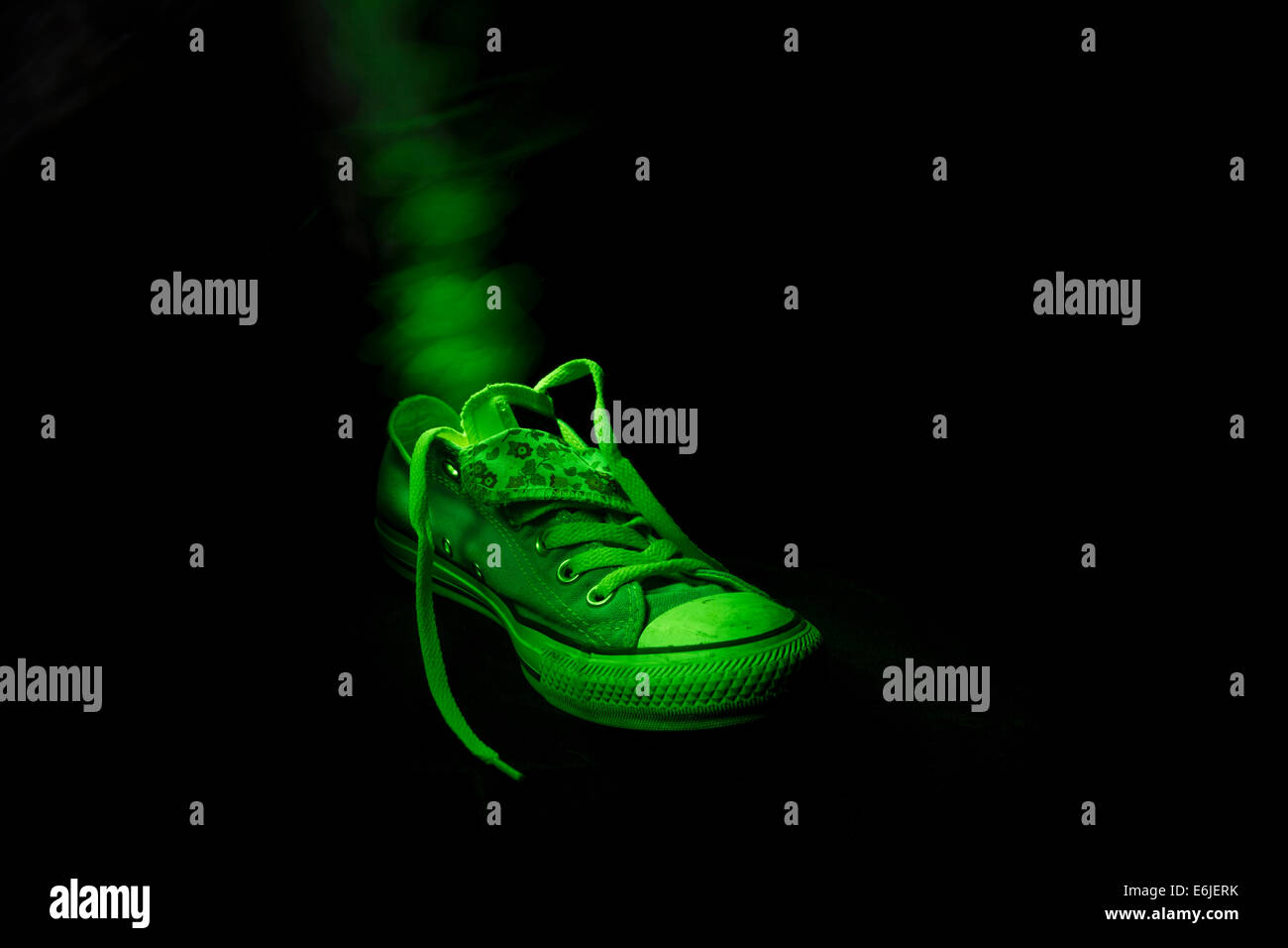Single old fashionable toxic training shoe in green light at night with visible odour Stock Photo