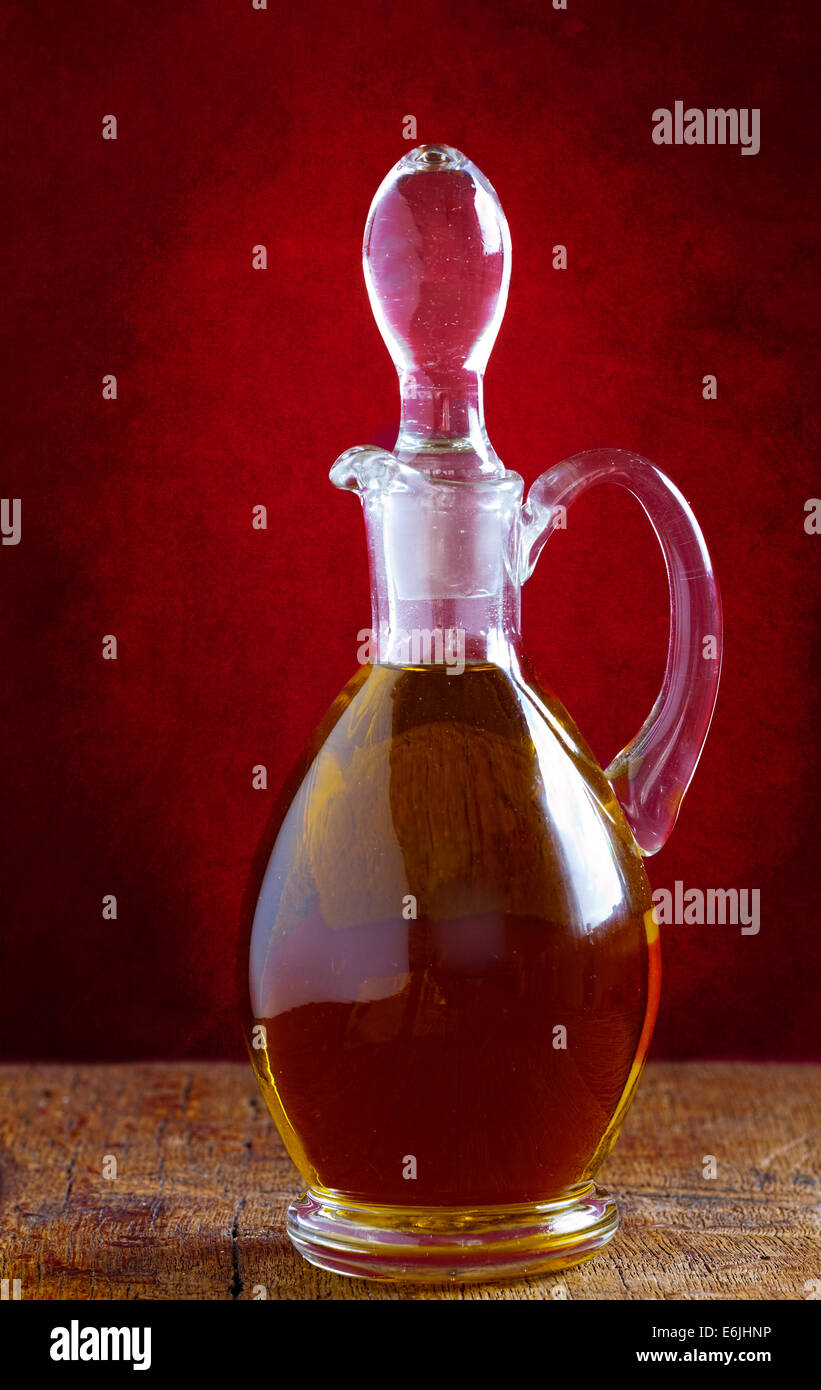 Glass carafe with olive oil on an old wooden table in front of a red wall in vintage style Stock Photo