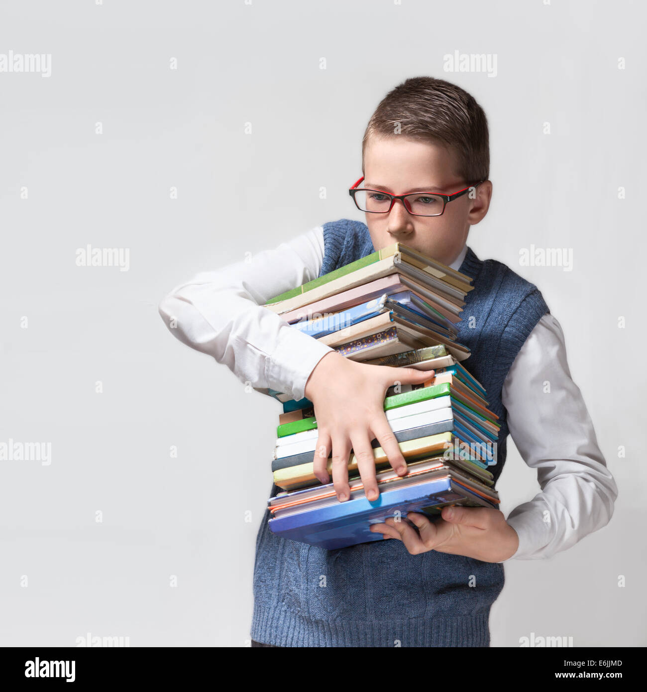 The cute smart schoolboy teenager in a glasses holds a heavy stack of books. Stock Photo