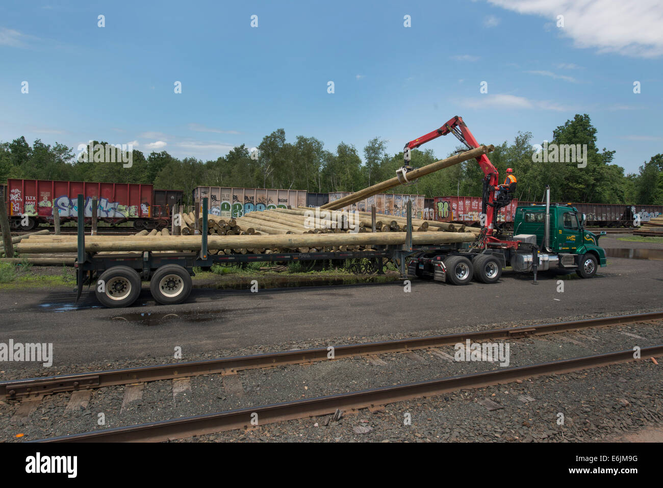Flat, or open bed truck fitted with knuckle boom for moving telephone poles, loading poles from rail yard. Anastasio Group Stock Photo