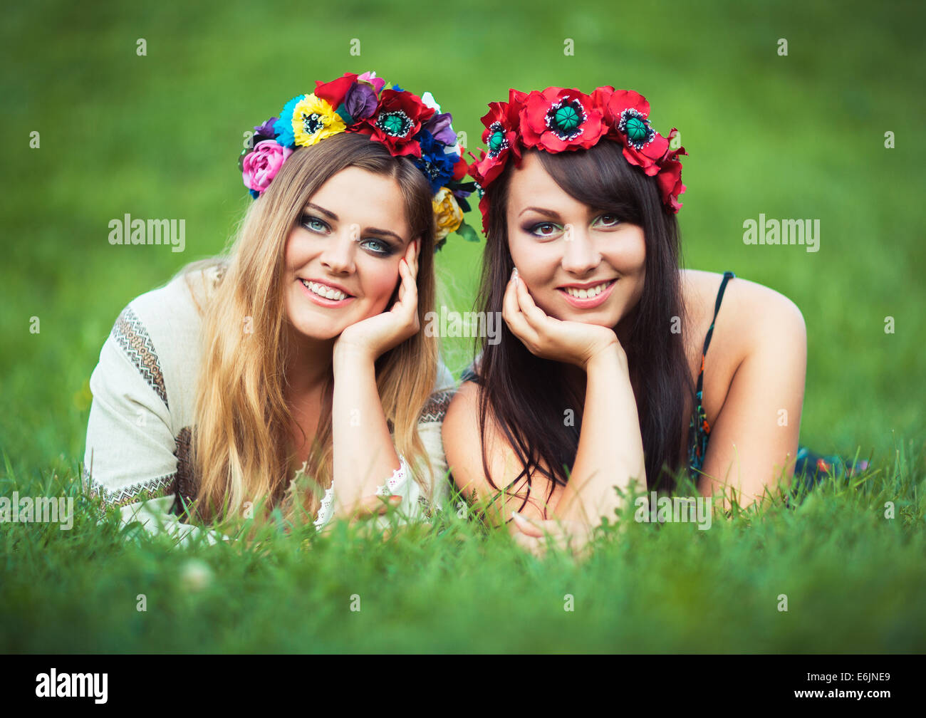 Two beautiful laughing girl in Ukrainian national costumes lie on the green grass Stock Photo