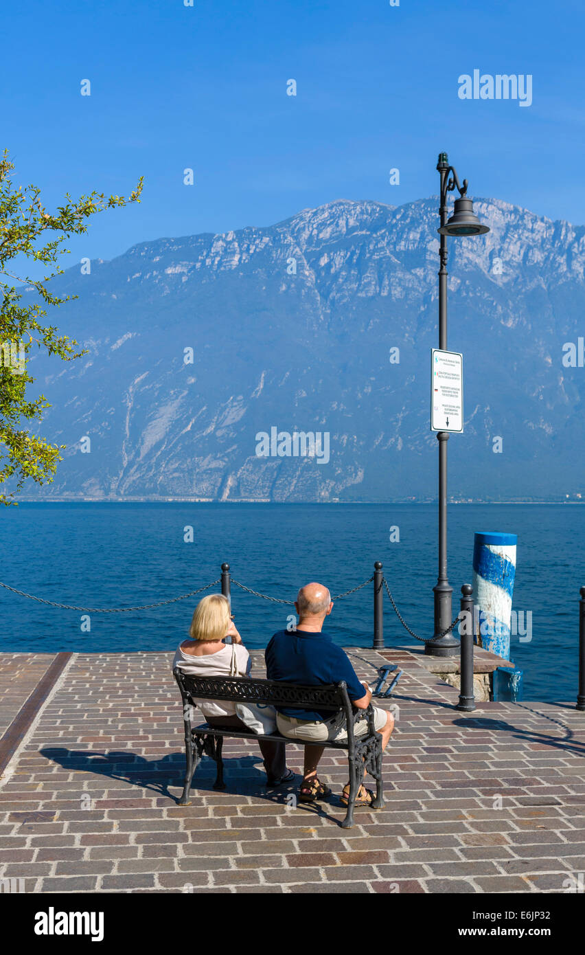 Middle aged couple sitting on the lakefront in Limone sul Garda, Lake Garda, Lombardy, Italy Stock Photo
