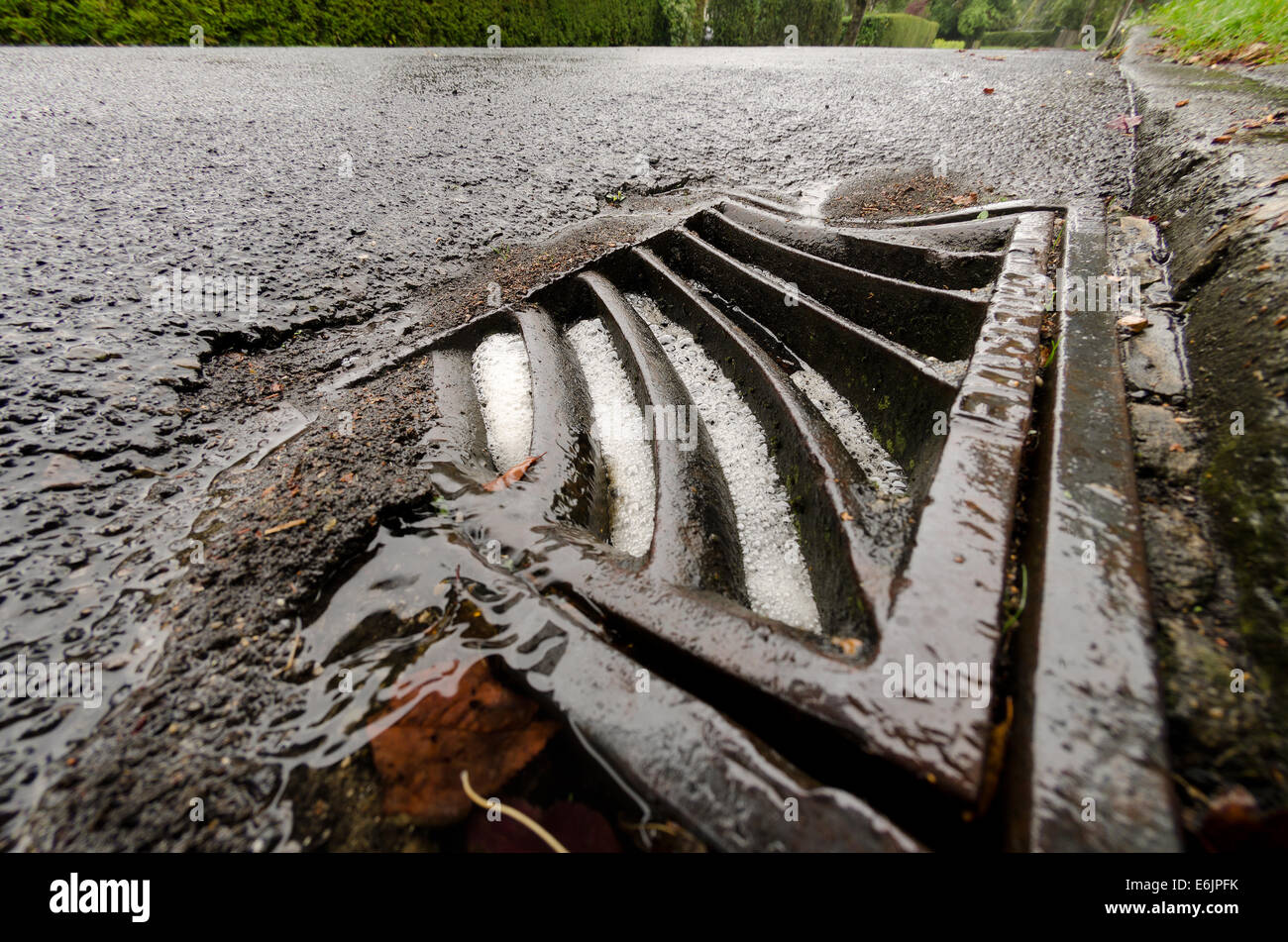 Blocked overflowing roadside drain tarmac highway leading to more surface water on empty roadway Stock Photo