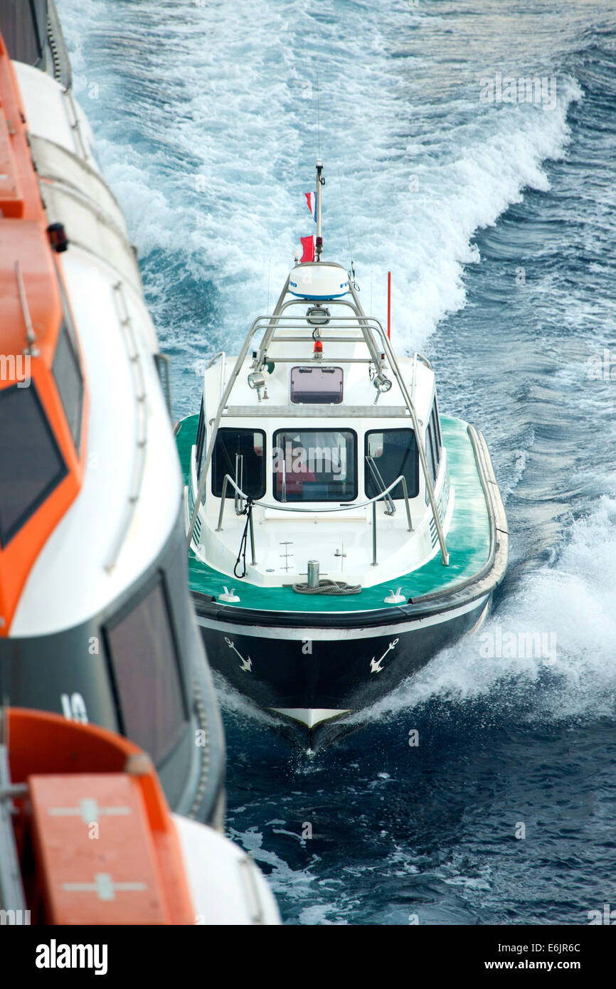 Pilot boat transporting the pilots between land and the outbound cruise ship Stock Photo