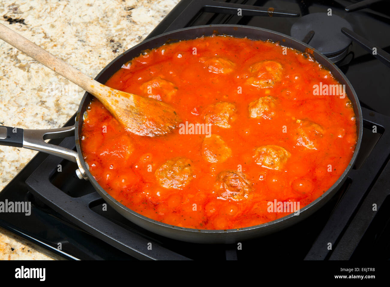 Spaghetti marinara sauce with delicious meatballs simmering in a sauce pan before being added to a pile of pasta. Stock Photo
