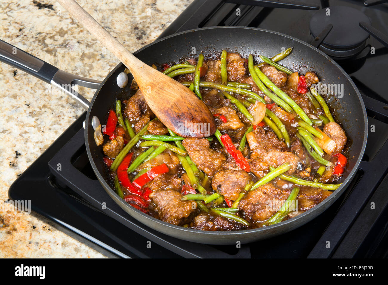 Fresh Asian style beef stir fry with green beans, peppers and onions simmering in a frying pan. Stock Photo