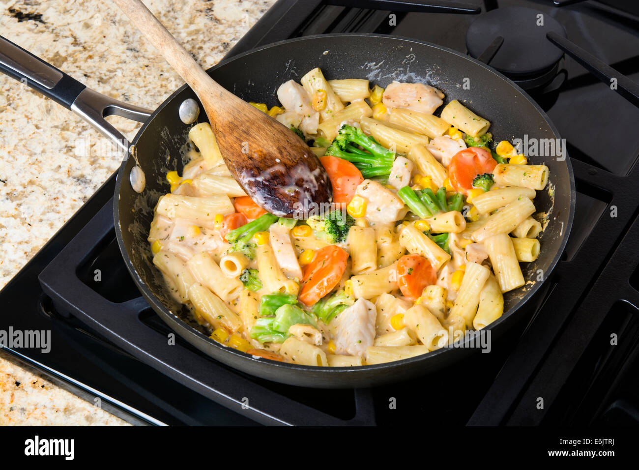 Freshly cooked pasta with vegetables, chicken and cream sauce in a stove top simmering pan Stock Photo