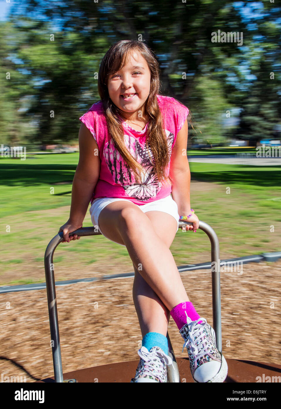Summer photograph of seven year old girl on a playground merry-go-round Stock Photo