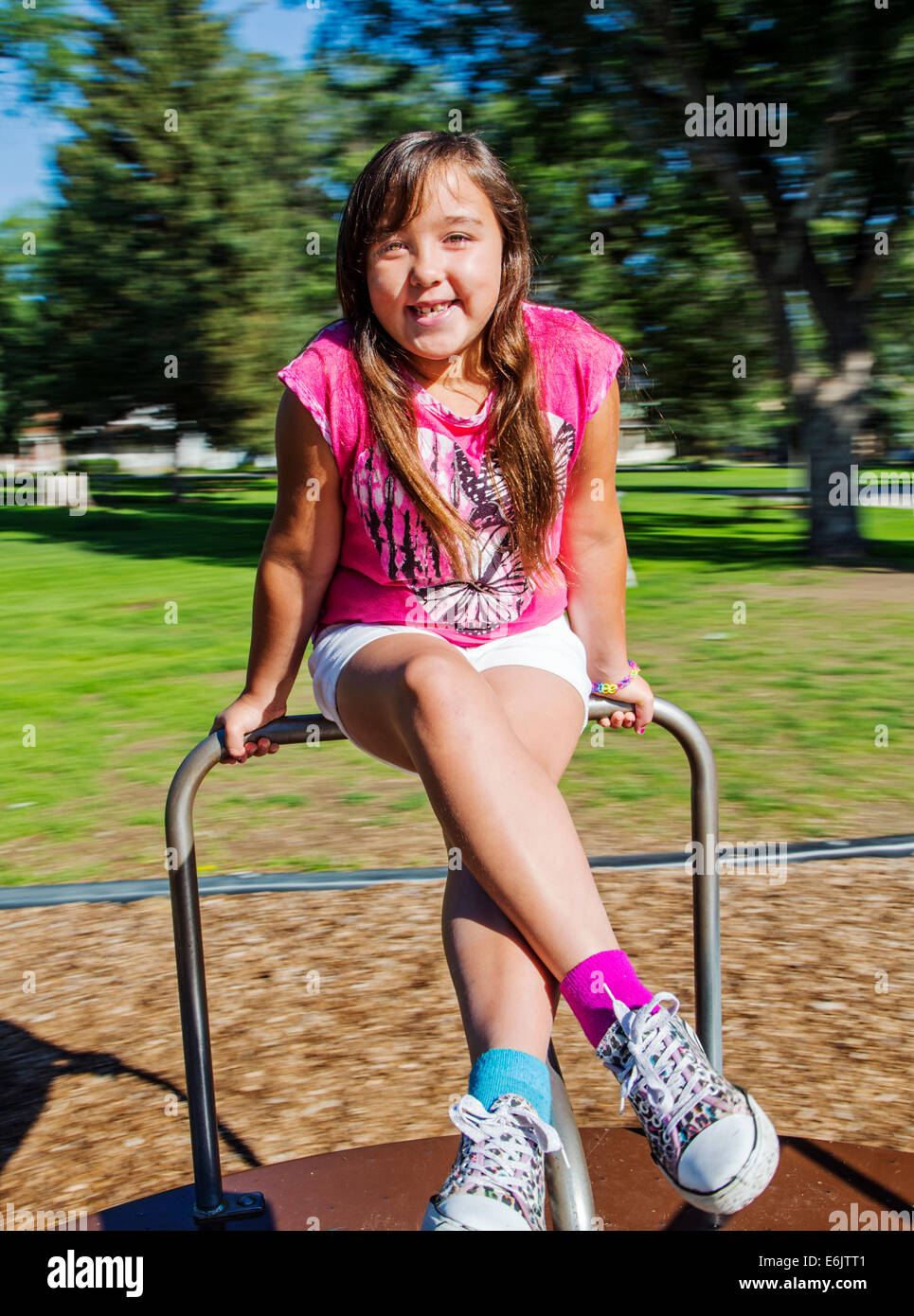 Summer photograph of seven year old girl on a playground merry-go-round Stock Photo