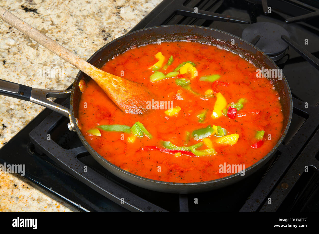 A simmering pan of marinara sauce with fresh, colorful peppers cooks to perfection before being poured over spagetti pasta. Stock Photo