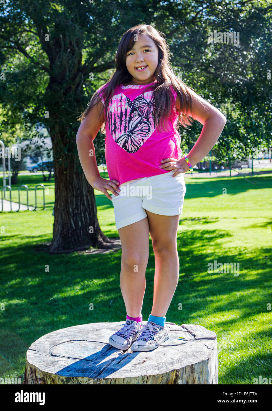 Summer portrait of seven year old girl posing on a large old tree stump in a park Stock Photo