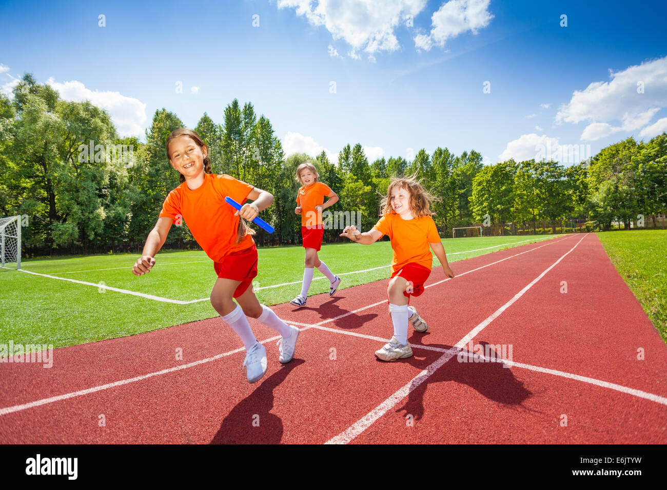 Three girls with one relay baton running Stock Photo