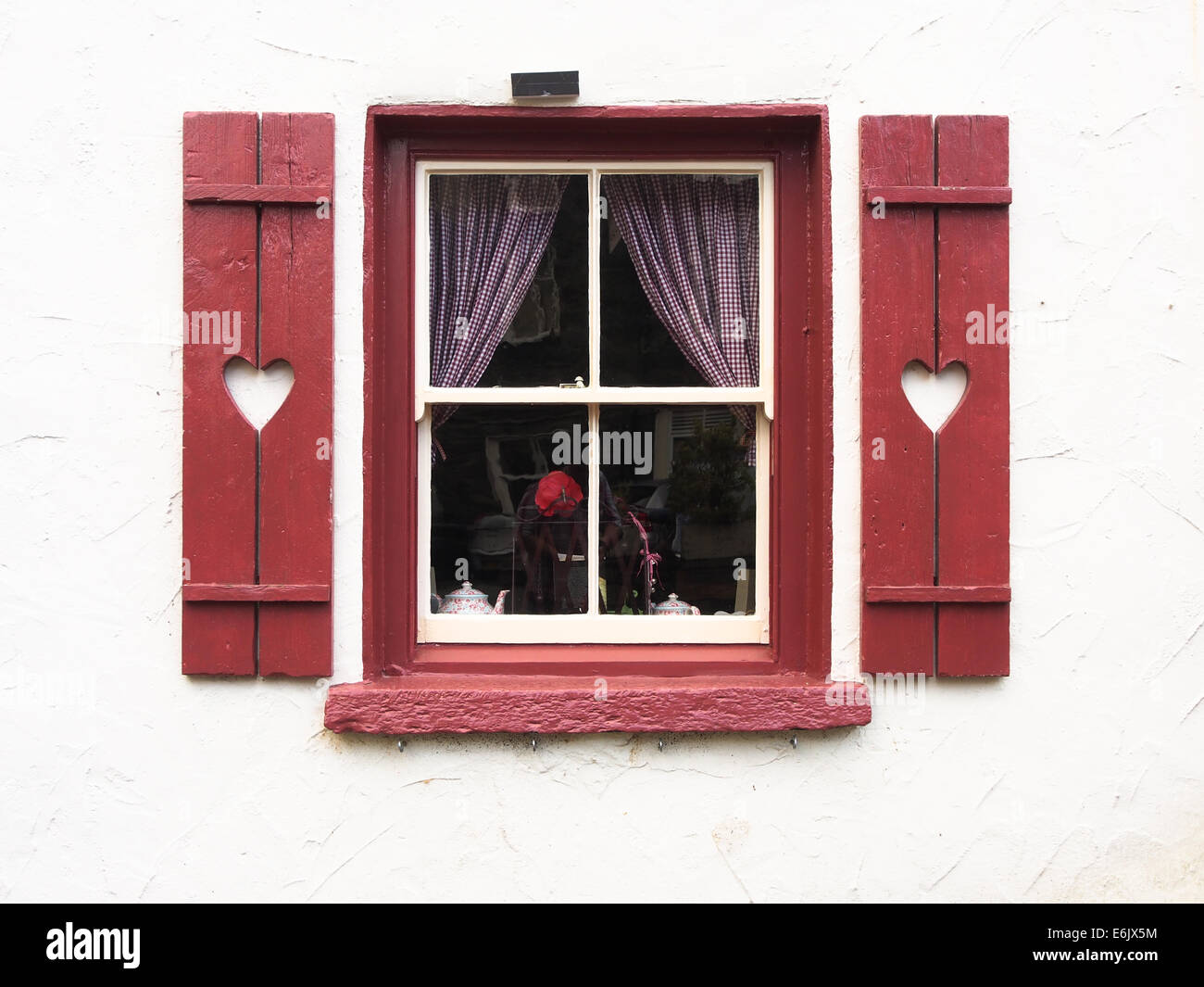 red window frame with red shutters and heart shapes surrounded by a white wall Stock Photo