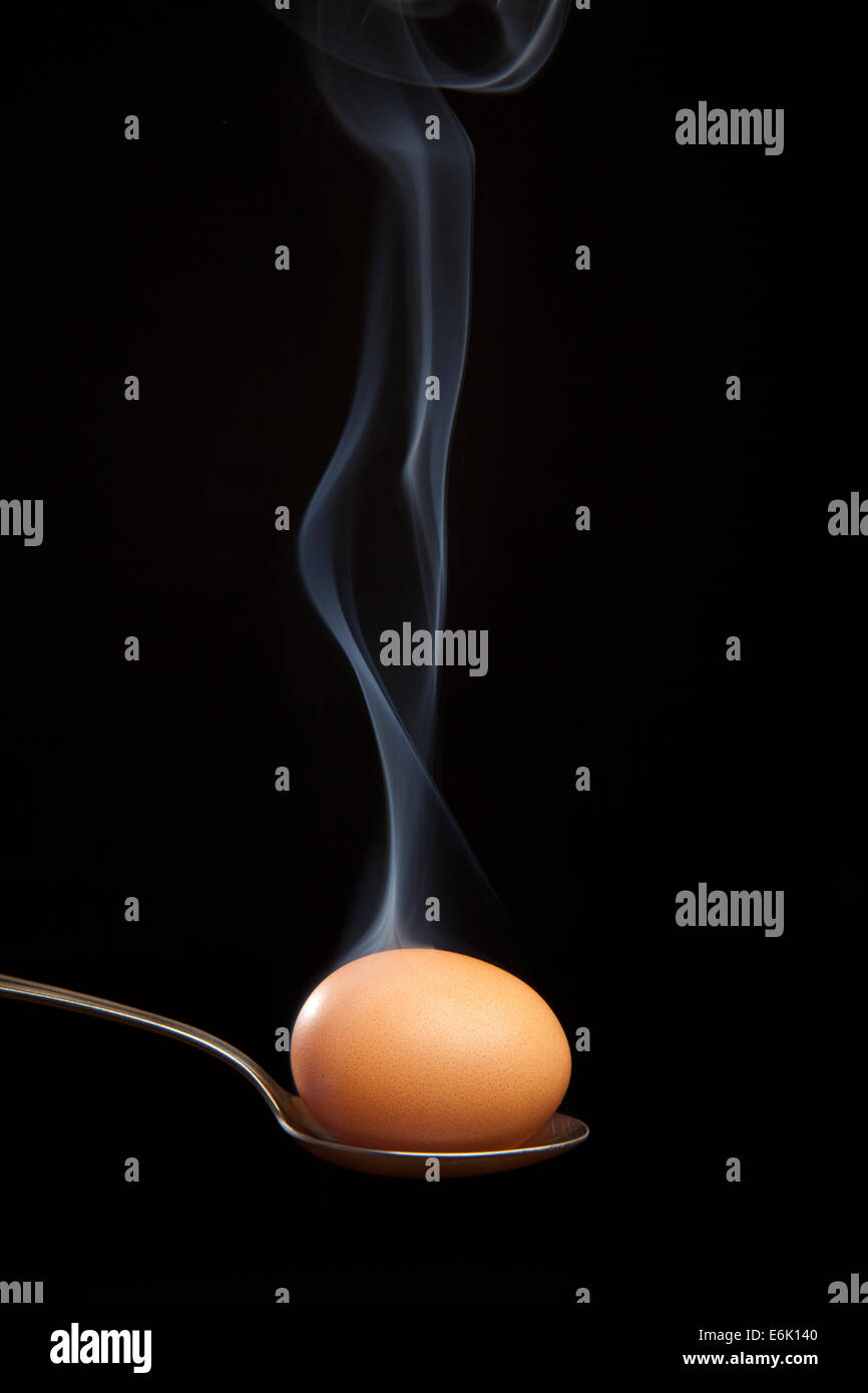 Brown egg wrapped in smoke in silver spoon Stock Photo