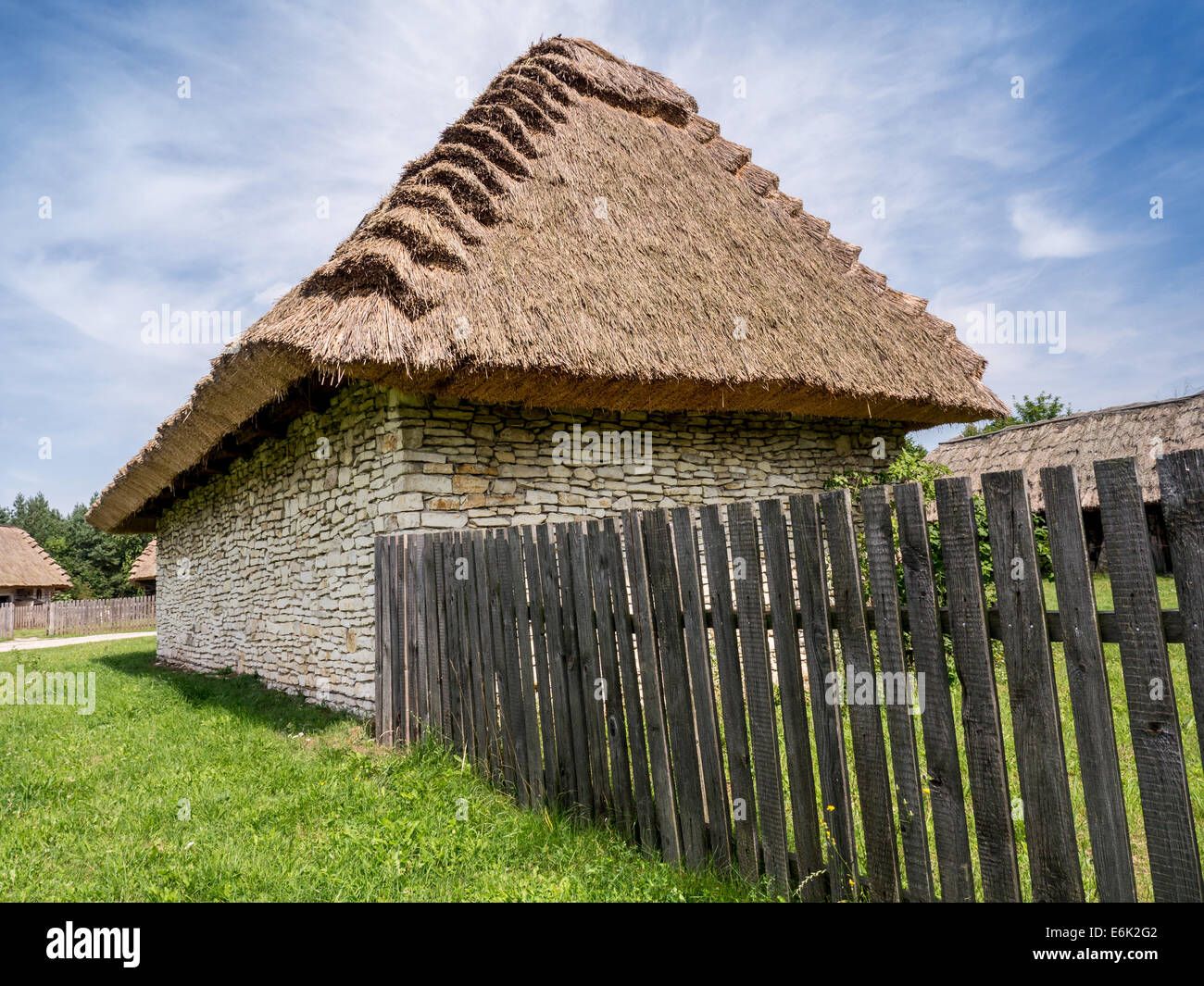Farmstead with thatched cottage and picket fence shot against blue sky Stock Photo