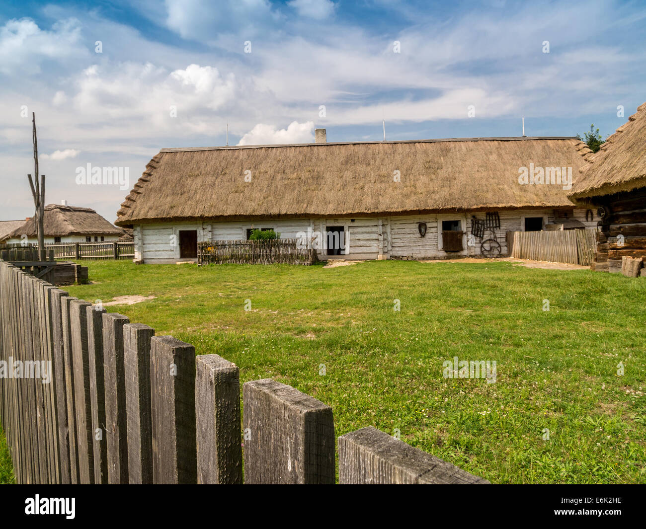 Old style Polish farmstead with thatched outbuildings and picket fence shot against blue sky Stock Photo