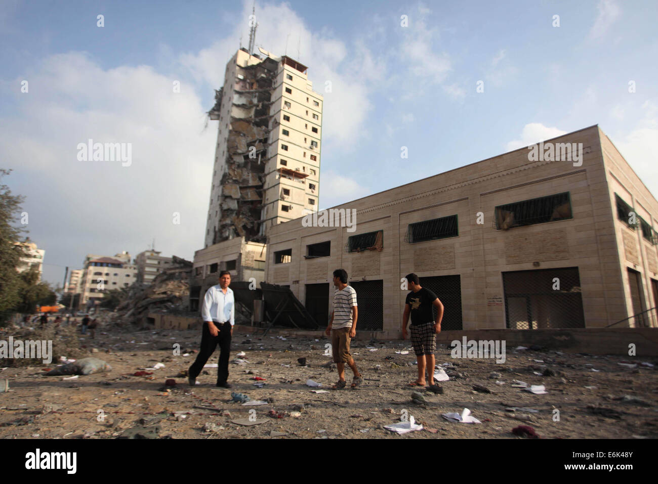 Gaza City, Gaza Strip, Palestinian Territory. 26th Aug, 2014. Palestinians stand next to the remains of one of Gaza's tallest apartment towers, which witnesses said was hit by an Israeli air strike that destroyed much of it, in Gaza City . Israeli air strikes launched before dawn on Tuesday killed two Palestinians and destroyed much of one of Gaza's tallest apartment and office buildings, setting off huge explosions and wounding 20 people. Credit:  ZUMA Press, Inc./Alamy Live News Stock Photo