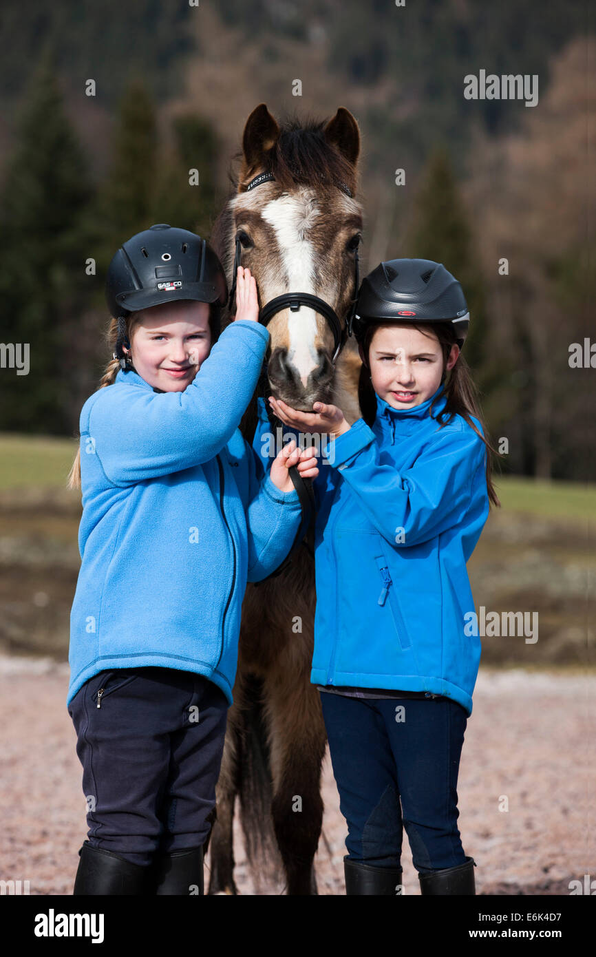 Two girls wearing riding helmets standing beside a pony, dun, with a bridle, Tyrol, Austria Stock Photo