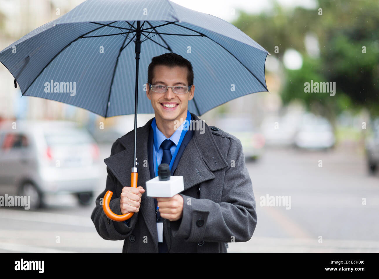 male news reporter holding umbrella and live broadcasting in the rain Stock Photo