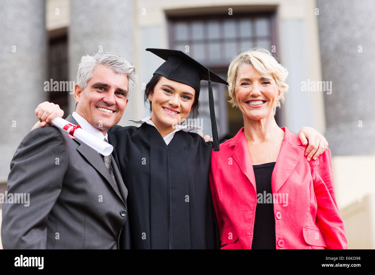 beautiful young female graduate with parents at ceremony Stock Photo