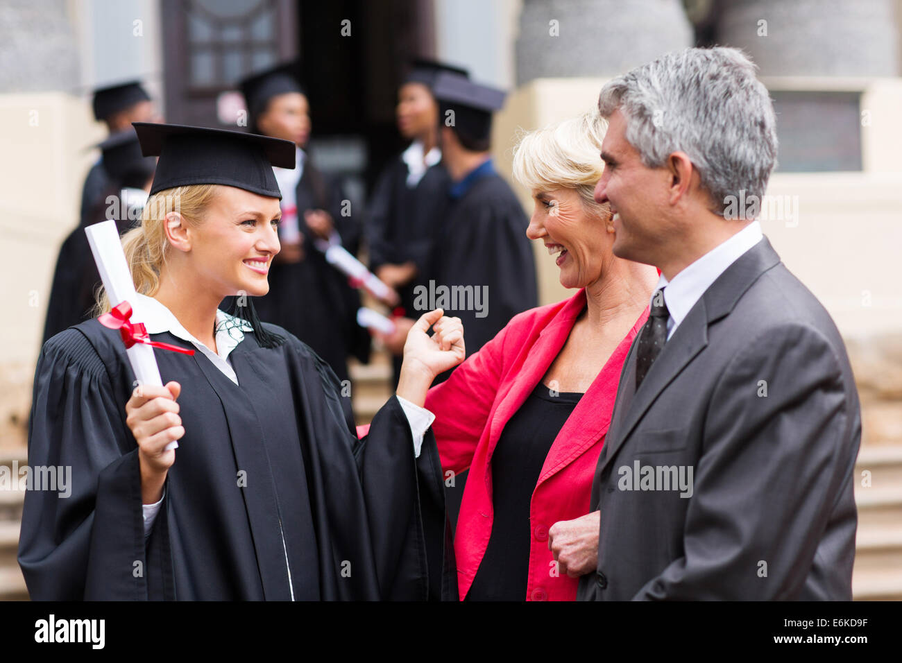 happy female university graduate with parents at graduation ceremony Stock Photo