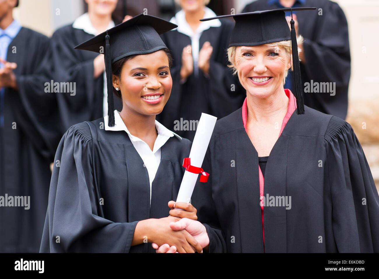 beautiful African female graduate handshaking with dean outside university Stock Photo