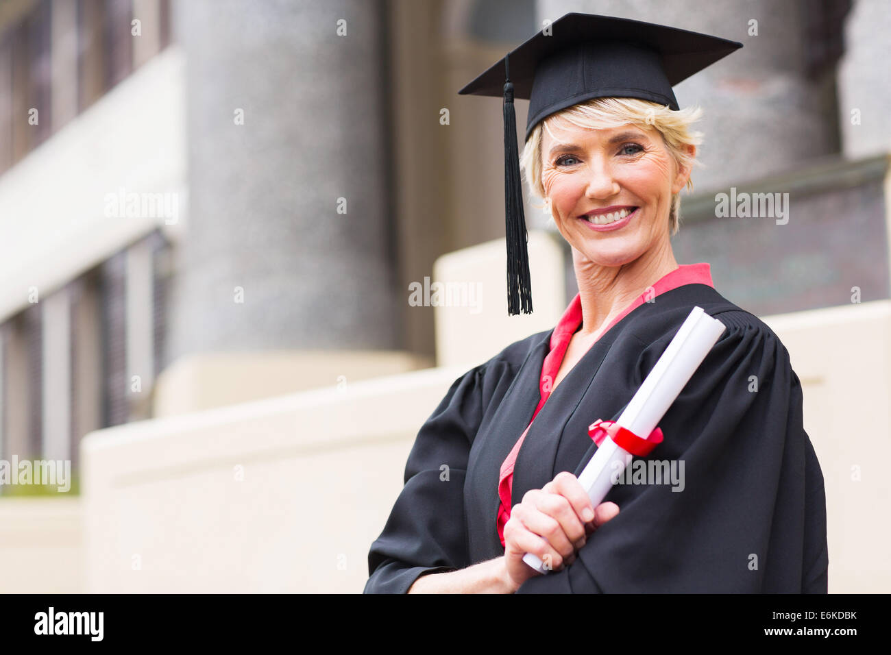 happy middle aged woman with graduation cap and gown holding diploma Stock Photo