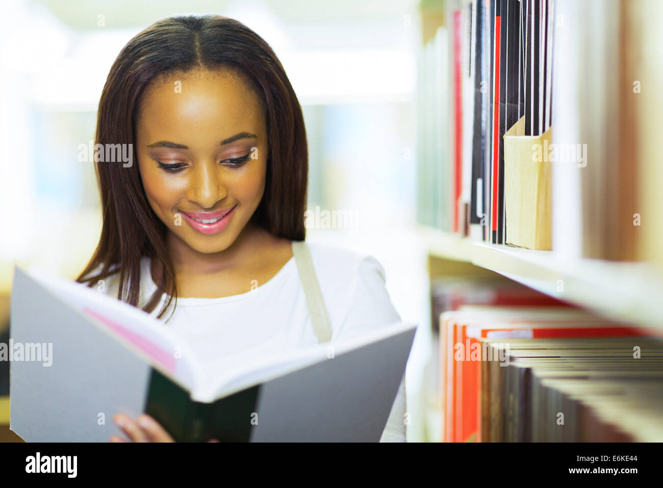 smiling female African American university student reading in library ...