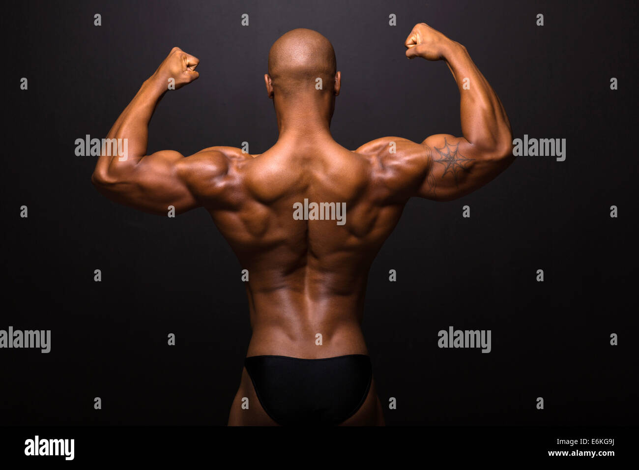 rear view of afro American male bodybuilder posing on black background ...