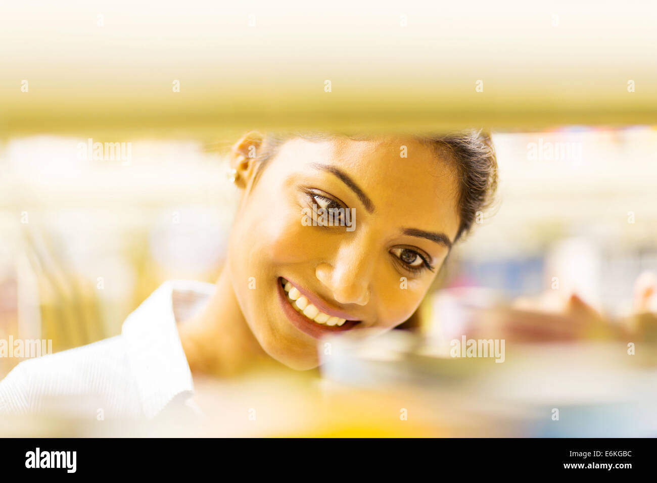 pretty Indian college student behind bookshelf in library Stock Photo
