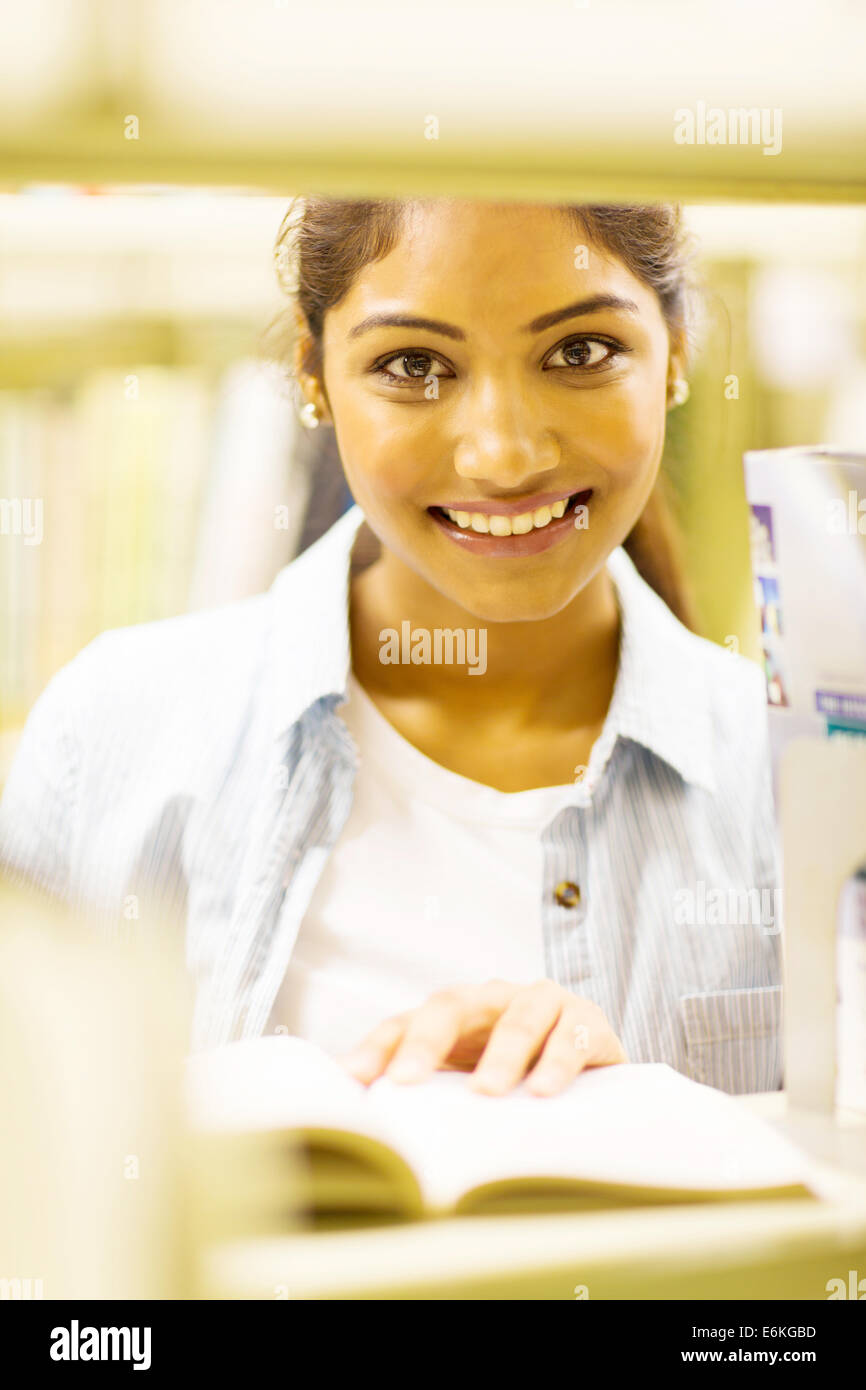 pretty female Indian college student reading book in library behind bookshelf Stock Photo